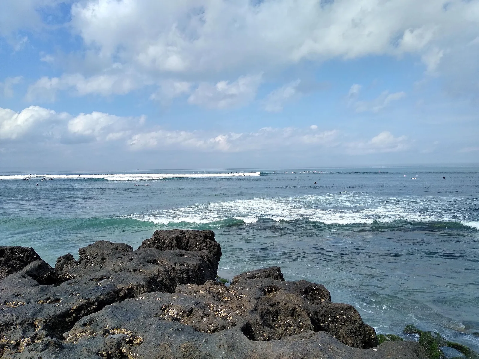Indian Ocean waves on the volcanic rock of Canggu beach, under a blue sky