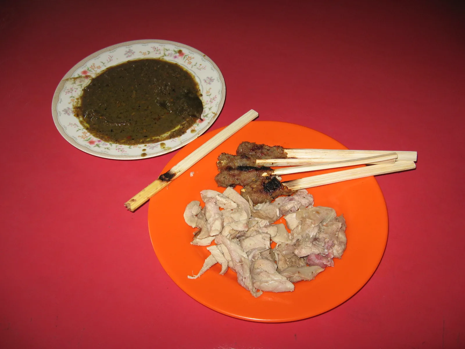 Plate of babi guling with skewers of sate lilit and a bowl of sauce