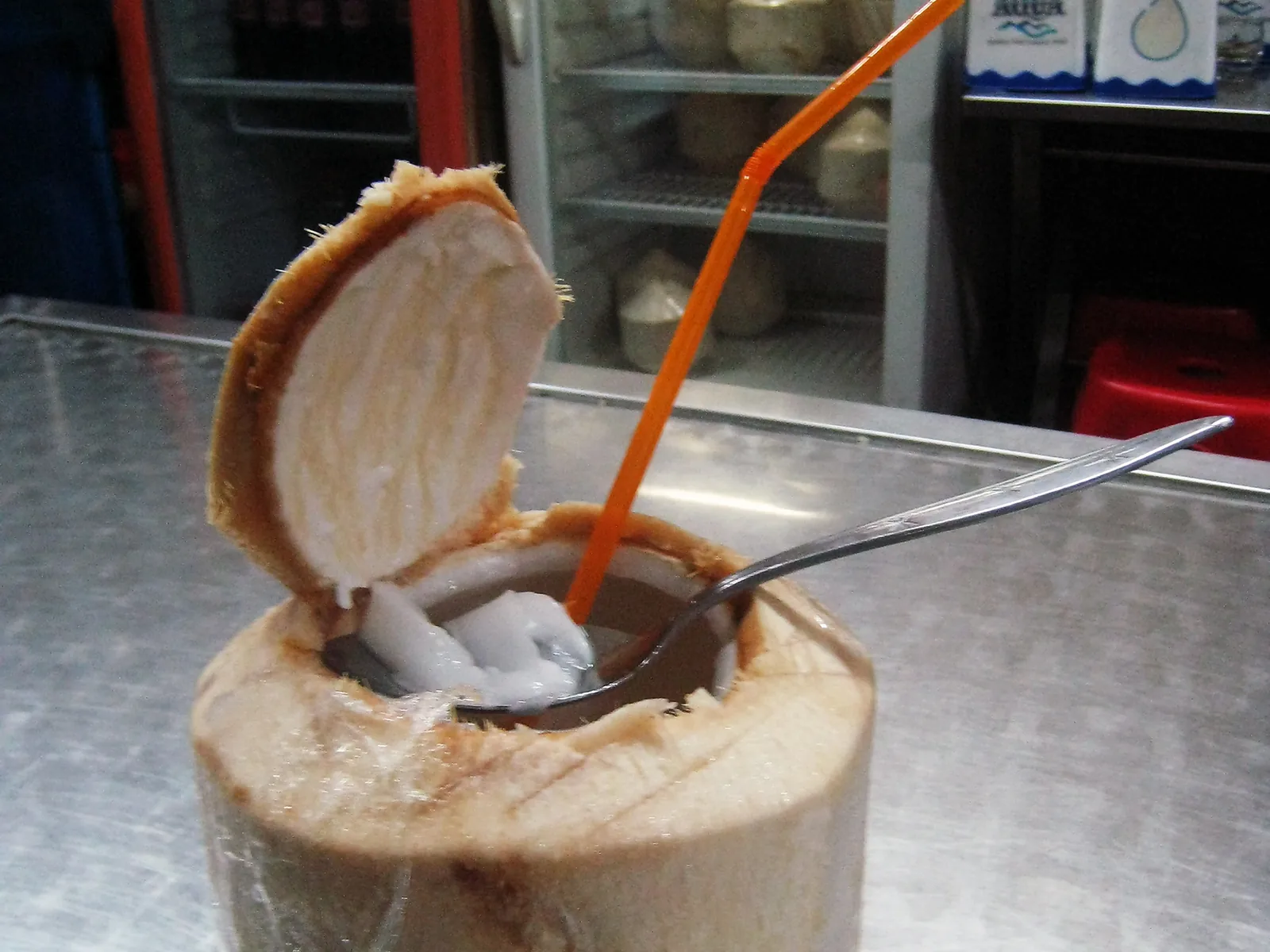 Opened coconut served with a straw, water and flesh inside