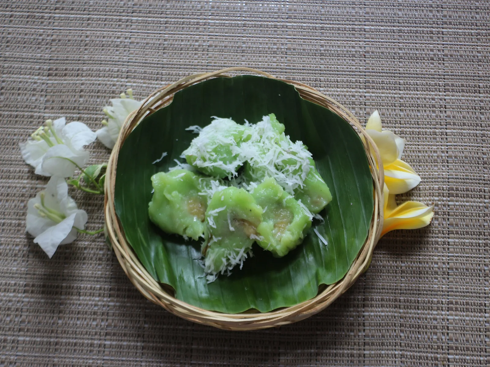 Green pisang rai rolled in grated coconut, in a basket on a banana leaf