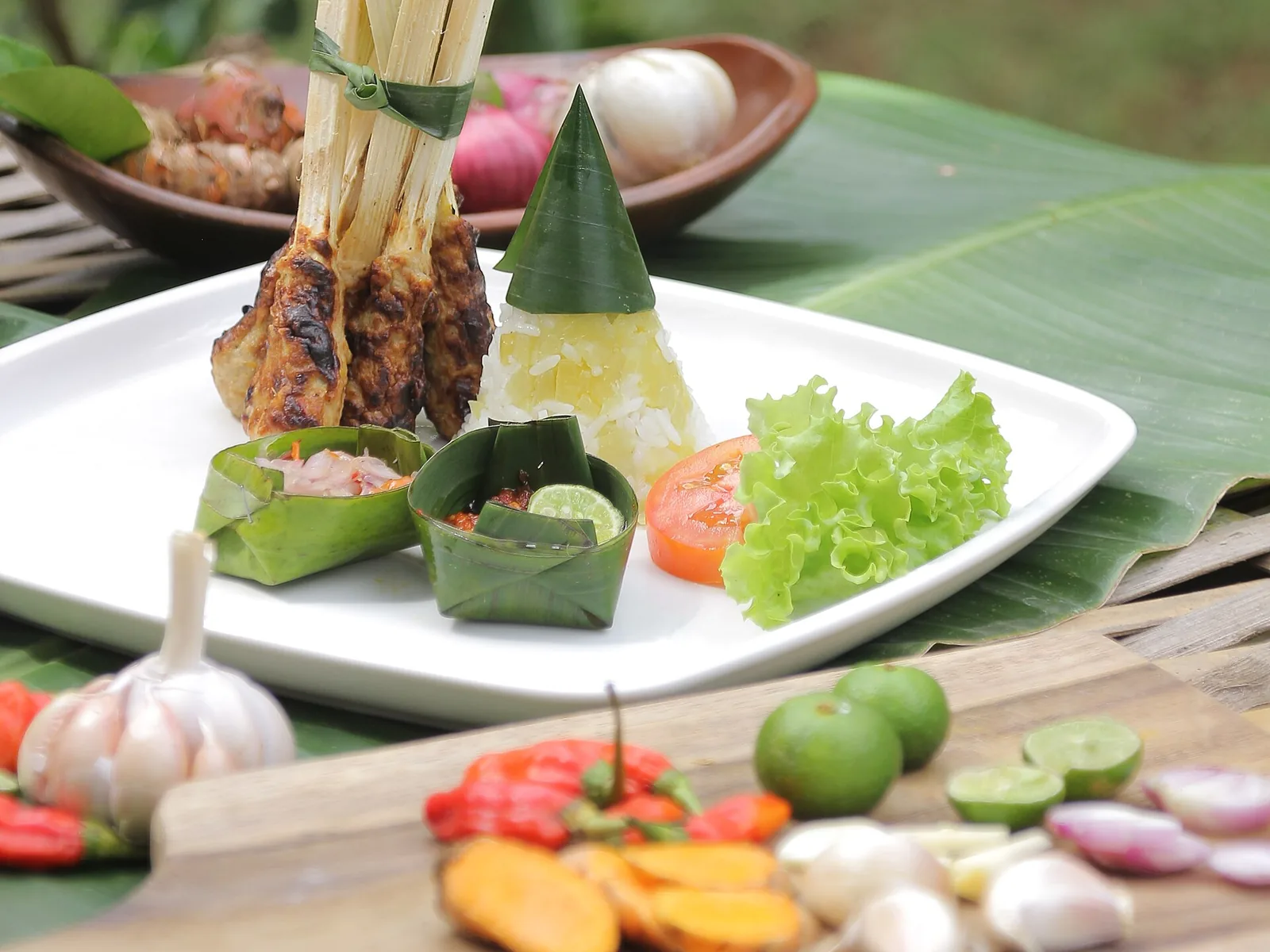 Grilled sate lilit on sticks, served with a cone of rice and sauces in banana-leaf cups
