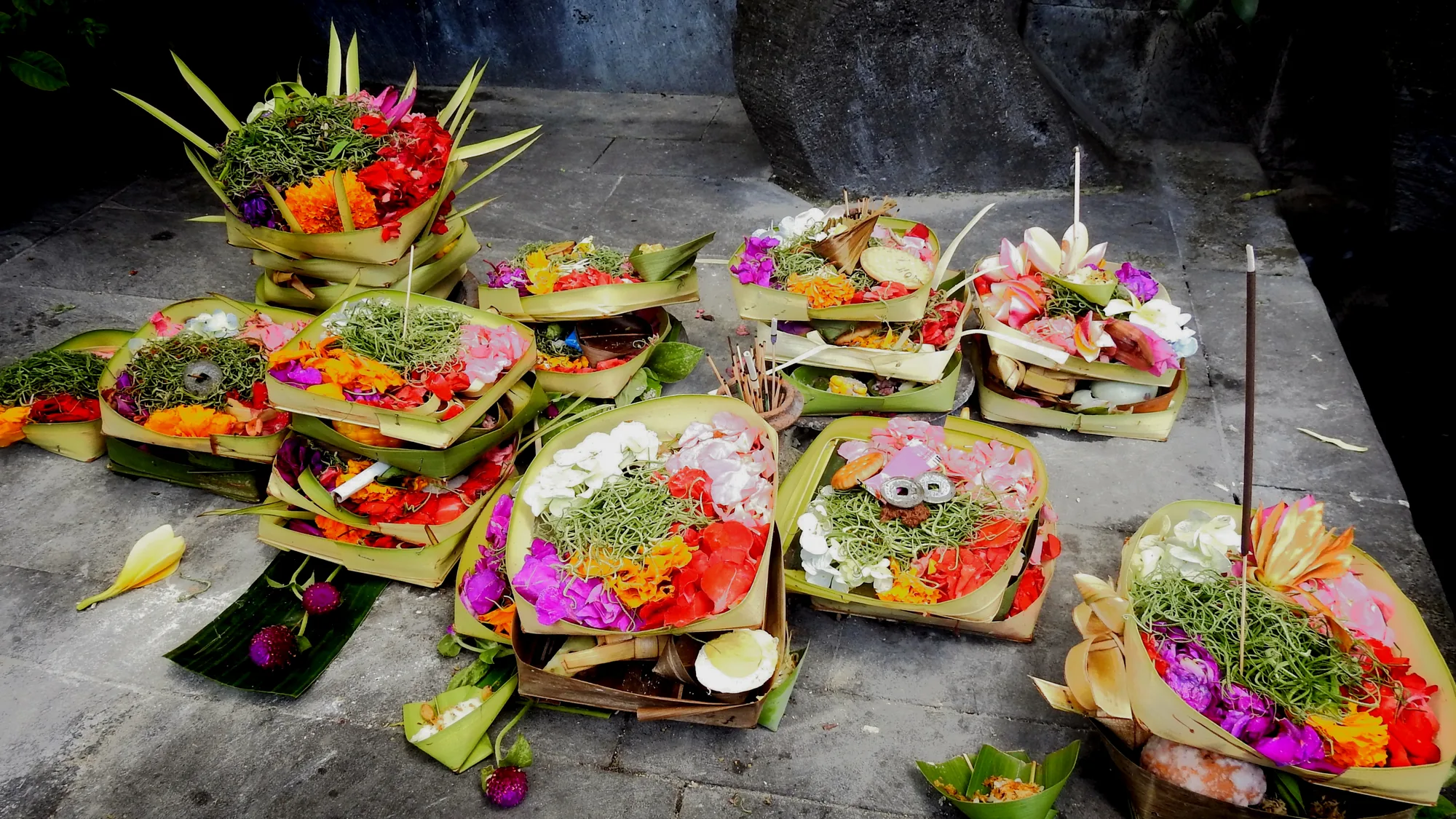 Canang sari placed on the stone floor in front of a carved, gilded wall, surrounded by petals
